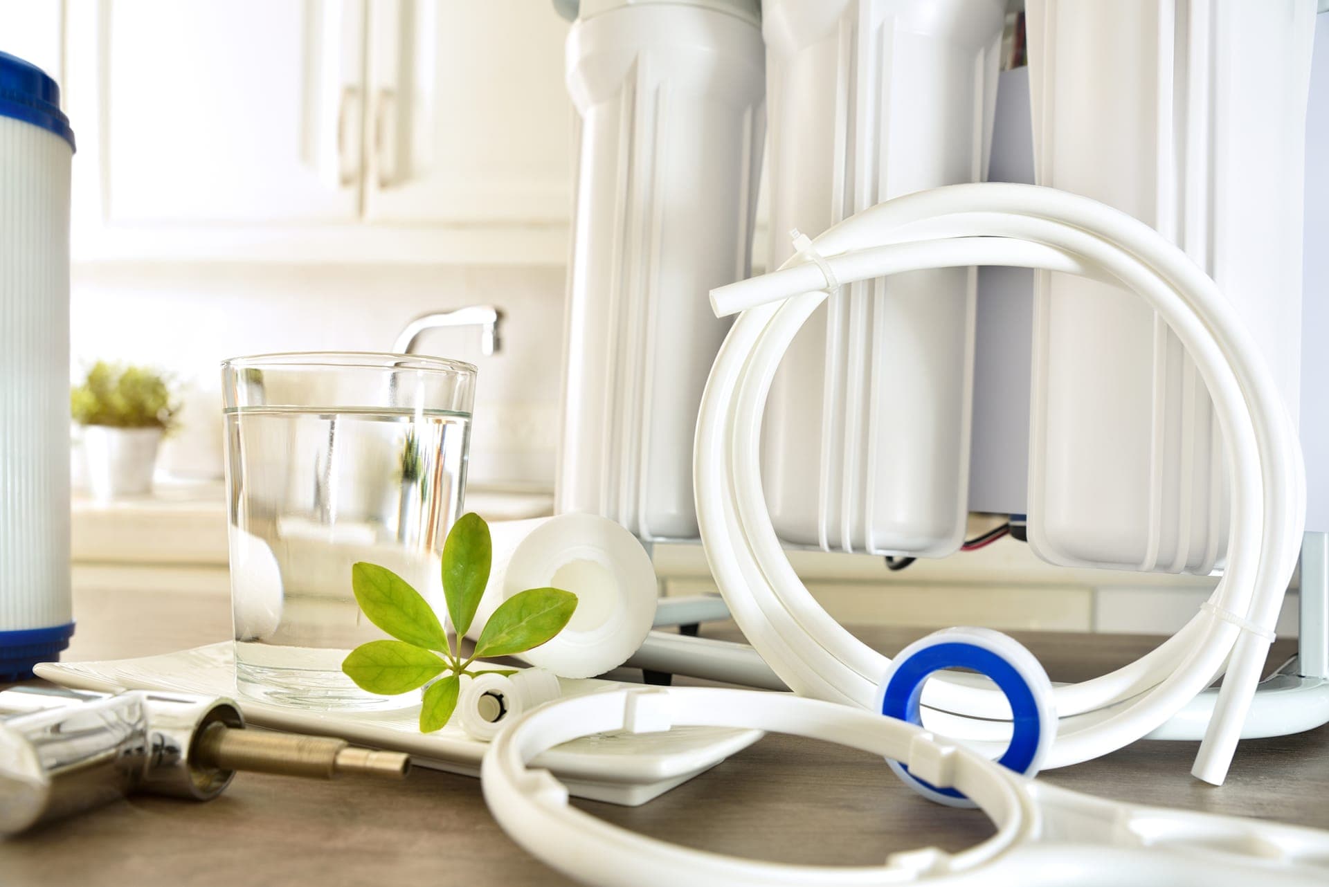 Multi-stage drinking-water filter system with spare cartridges, tubing, and a glass of water on a kitchen counter