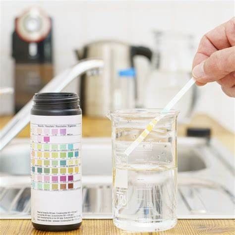 Water test strip compared with a color chart beside a sample